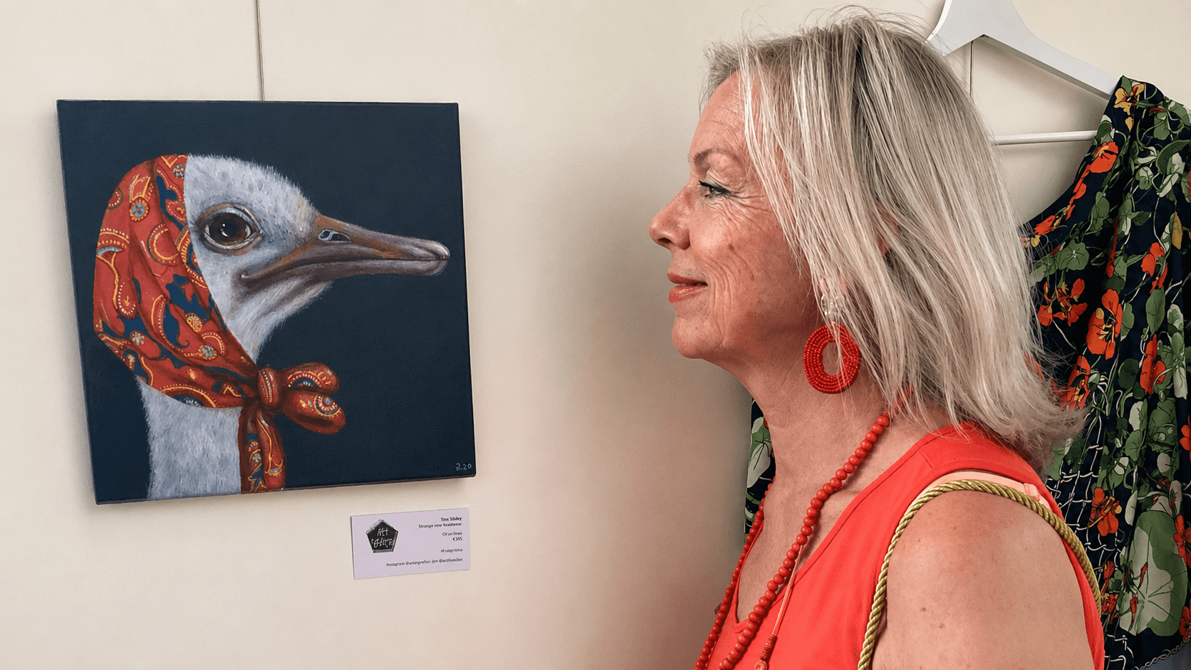 Ilse Nicola bekijkt een van haar schilderijen, een struisvogel met een sjaal om, tijdens een expositie